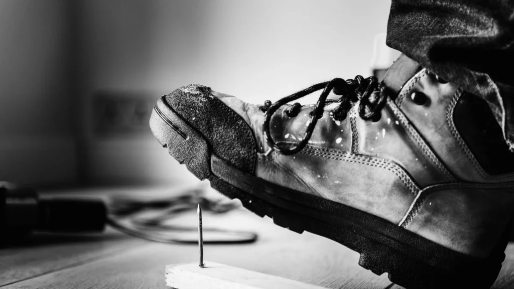 Industrial safety shoe with puncture-resistant sole stepping on a nail to demonstrate workplace foot protection in UAE construction environments.